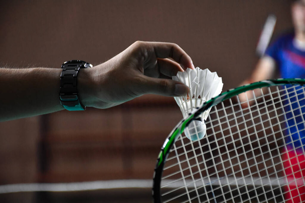 Men single badminton player holds racket and white cream shuttlecock in front of the net before serving it to another side of the court, soft and selective focus. - Foto, imagen