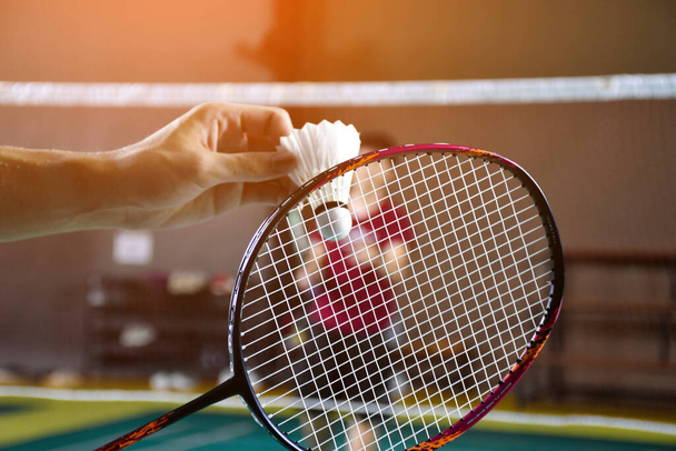 Uomini giocatore badminton singolo tiene racchetta e bianco navetta crema davanti alla rete prima di servirlo ad un altro lato della corte, messa a fuoco morbida e selettiva. - Foto, immagini