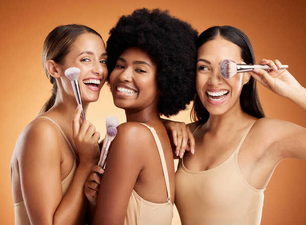 Makeup, beauty and women with brush for cosmetics against a brown mockup studio background. Face portrait of happy, smile and young model group with product for facial foundation and skincare. - Photo, Image