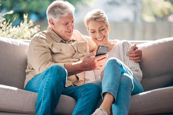 Otthon, édes honlap. egy boldog idős pár okostelefont használ otthon a kanapén, - Fotó, kép