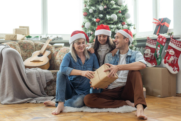 Рождественская семья Счастье. Портрет отца, мамы и дочери дома возле елки, все улыбаются. - Фото, изображение