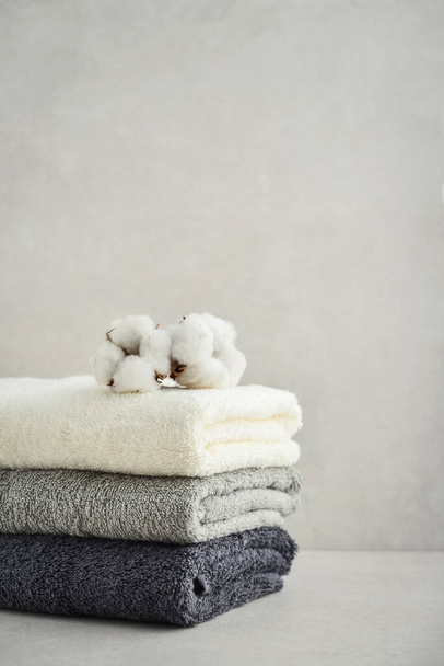 Stack of bath towels with cotton flowers on light concrete background closeup - Photo, image