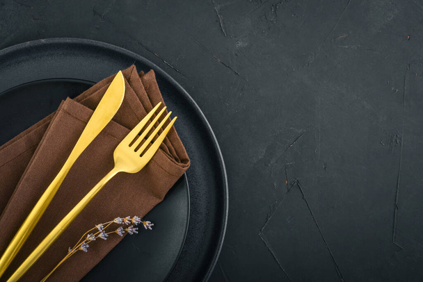 Modern minimal table place setting with black plates and golden cutlery on black  background top view. Space for text . Modern kitchen. - 写真・画像