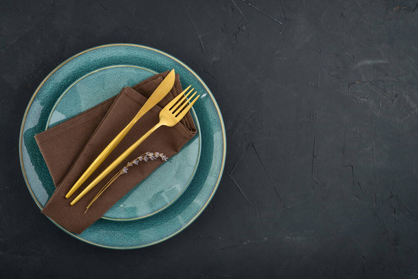 Modern minimal table place setting with blue plates and golden cutlery on black  background top view. Space for text . Modern kitchen. - Фото, зображення