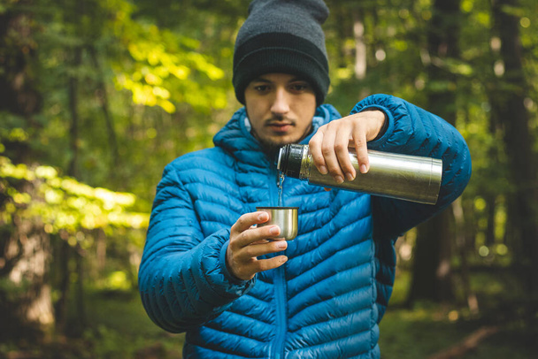 El excursionista en un largo sendero descansa y vierte el té caliente de un termo en una taza para calentar y reponer vitaminas y líquidos. Senderismo de alta montaña. - Foto, imagen