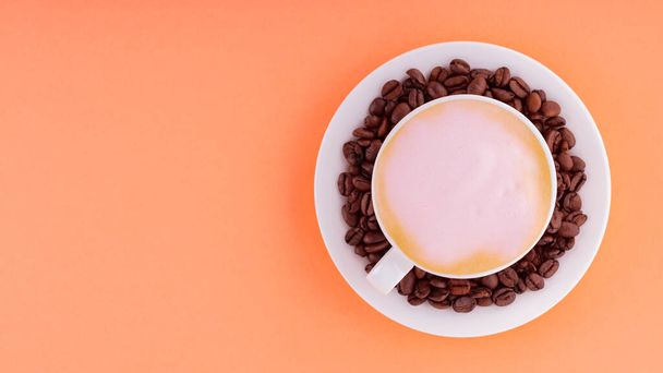 Cup of coffee with pink foam on a coral background. Coffee cup and roasted coffee beans on a saucer. Top view. Copy space - Foto, afbeelding