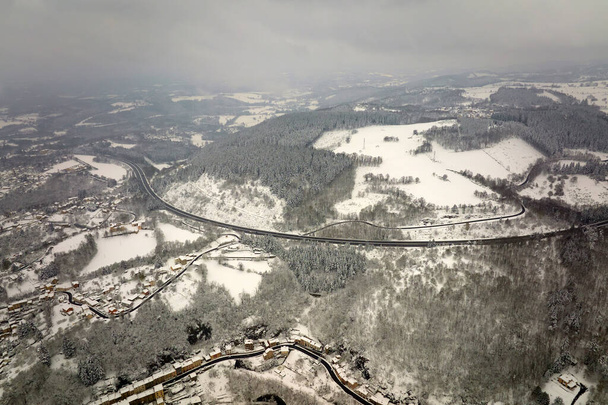 Aerial foggy landscape with mountain road covered with fresh fallen snow during heavy snowfall in winter mountain forest on cold quiet day. - Photo, Image