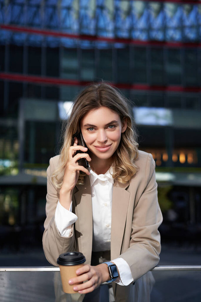 Plan vertical de femme d'affaires souriante répondre à un appel téléphonique mobile, parler sur smartphone et boire du café. - Photo, image