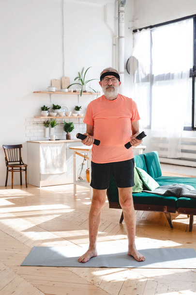 Hombre mayor haciendo ejercicio físico en casa con pesas - personas mayores y salud de bienestar - Foto, imagen