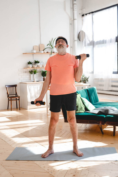 Elderly aged male exercising with dumbbells during online training. Old person man pensioner healthy training healthcare sport at home exercising fitness activity elderly age - Foto, Bild