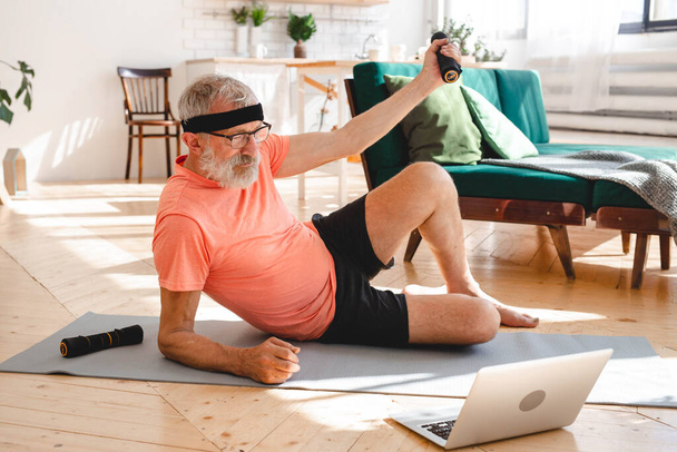 Seniorchef macht Fitnessübungen mit virtuellem Kurs und hält Hanteln - Wohlbefinden und Wellness - Foto, Bild