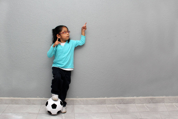 Grelha latina pobre de 4 anos joga com uma bola de futebol muito animado que ela vai ver a Copa do Mundo na pobreza - Foto, Imagem