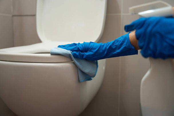 Trabajador sosteniendo spray para limpiar superficies y trapo, limpiando el inodoro en el baño - Foto, imagen