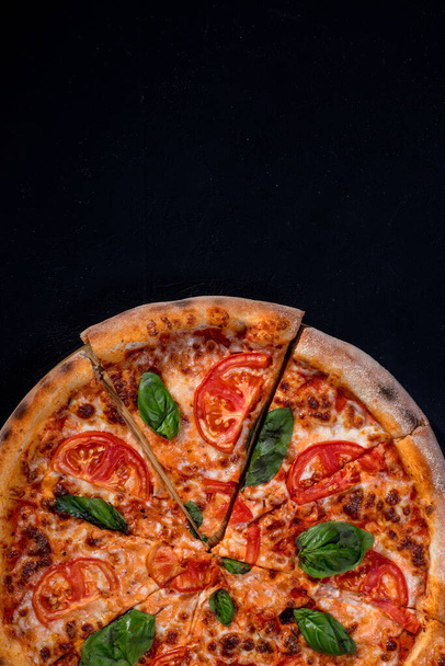 Delicious fragrant pizza-Margherita with mozzarella, tomatoes and basil on tomato sauce on black background. - Foto, Bild