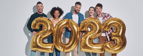 Group of young beautiful people in casual clothing carrying gold colored numbers and smiling while standing against gray background - Fotó, kép