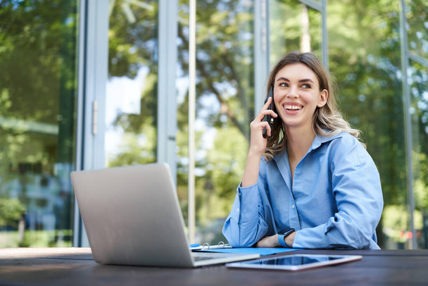 Retrato de vendedora trabalhando fora no ar fresco, perto do prédio de escritórios. Sorrindo mulher corporativa com laptop, fazendo telefonema. - Foto, Imagem