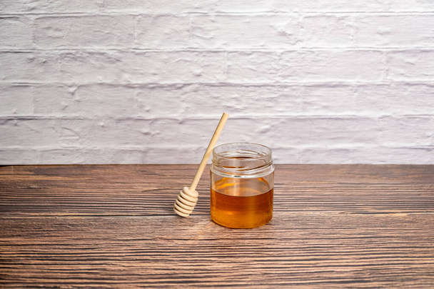 Pot de miel et bâton de bois isolé mur de briques blanches - Photo, image