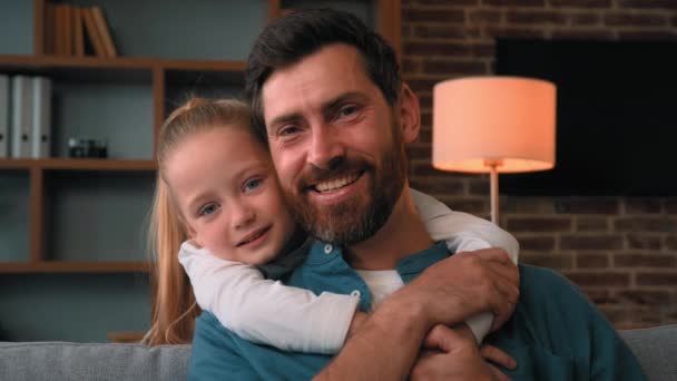 Cheerful dad piggybacking happy child daughter at home family portrait beautiful preteen girl hug tightly handsome brunet single father male parent looking at camera laughing young fatherhood concept - Footage, Video