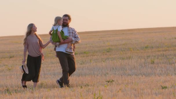 Boční pohled Kavkazští rodiče s dětskou dívkou v parku. Rodina matka otec s dcerou chůze podél pšeničného pole ve venkovské krajině venku spolu cestování odpočinek mluvení jít pěšky na žluté trávě - Záběry, video