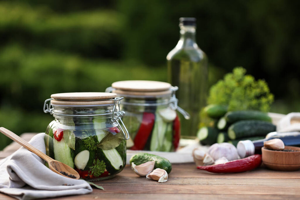 Jars of delicious pickled cucumbers and ingredients on wooden table against blurred background. Space for text - Foto, afbeelding
