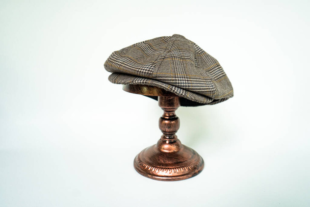 Detail of a classic eight-panel newsboy hat, in dark brown herringbone tweed fabric set against a bronze head mannequin on a white background - Foto, Imagem