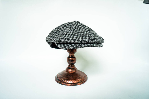 Detail of a classic eight-panel newsboy hat, in black and white pattern herringbone tweed fabric set against a bronze head mannequin on a white background - Фото, изображение