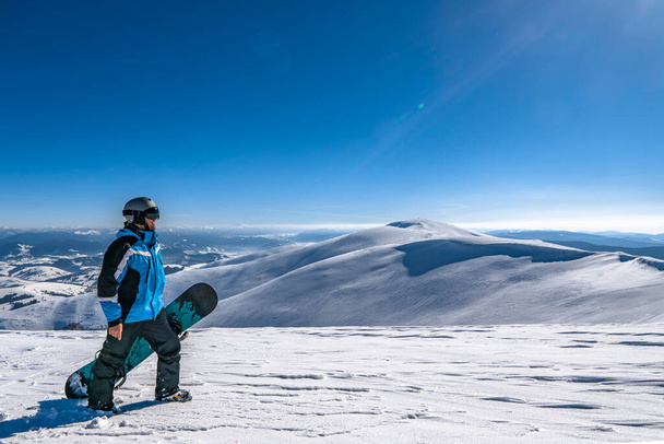 Snowboarder with snowboard in hand on mountain top. Winter freeride snowboarding - Fotoğraf, Görsel