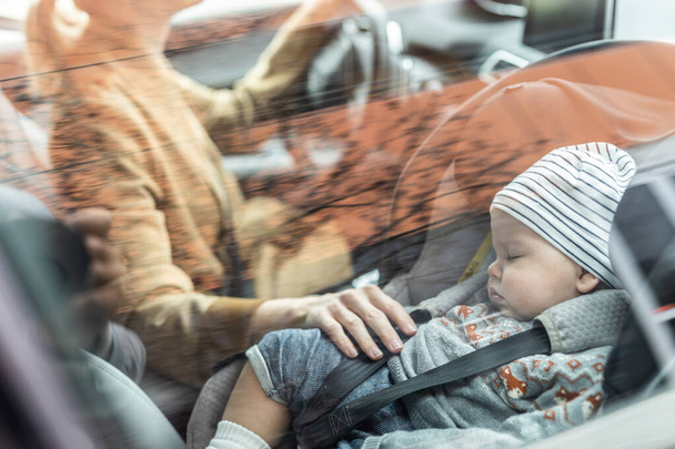 Matka koncentruje się na prowadzeniu samochodu rodzinnego na posyłki, podczas gdy jej dziecko śpi w foteliku dla niemowląt przy jej stronie - Zdjęcie, obraz