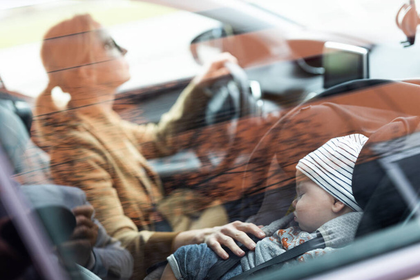 Matka se soustředí na řízení rodinné auto běží pochůzky, zatímco její dítě spí v kojenecké autosedačce u jejích stránek - Fotografie, Obrázek