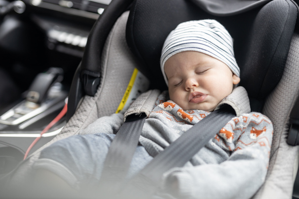 Niedlicher kleiner Junge schläft während Autofahrt in Babyschale im Beifahrerabteil geschnallt - Foto, Bild