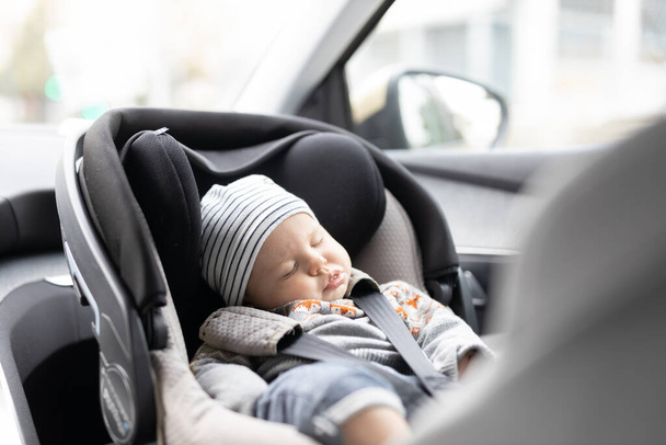Cute little baby boy sleeping strapped into infant car seat in passenger compartment during car drive - Photo, Image