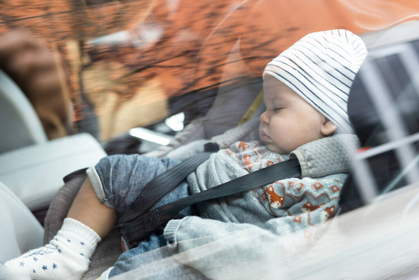Schattig klein jongetje slapend vastgebonden in kinderzitje in passagierscompartiment tijdens autorijden - Foto, afbeelding