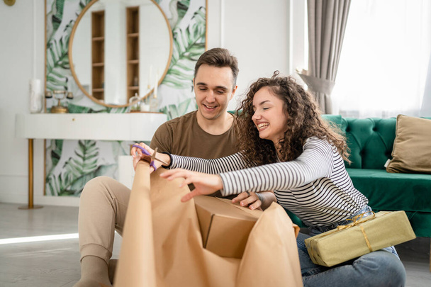 Couple homme et femme préparer des cadeaux pour les vacances caucasien mâle et femelle emballage cadeaux pour les amis en utilisant papier d'emballage heureux sourire tenir boîte cadeau à la maison les gens réels copier l'espace - Photo, image