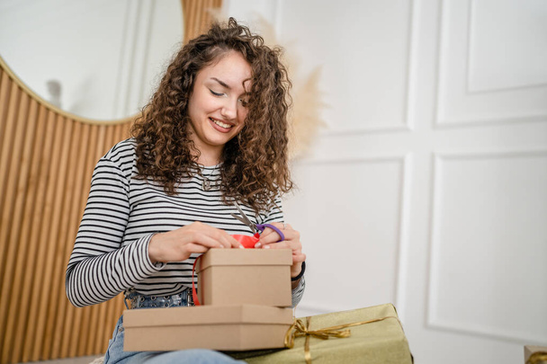 одна молодая женщина обернуть подарки дома счастливая женщина улыбка, держа оберточную бумагу и подарочную коробку подготовиться к упаковке подарков для праздничного сезона счастливая улыбка копировать пространство реальных людей - Фото, изображение
