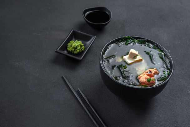 Traditional Asian soup on a black background. Miso soup with salmon. - Photo, Image