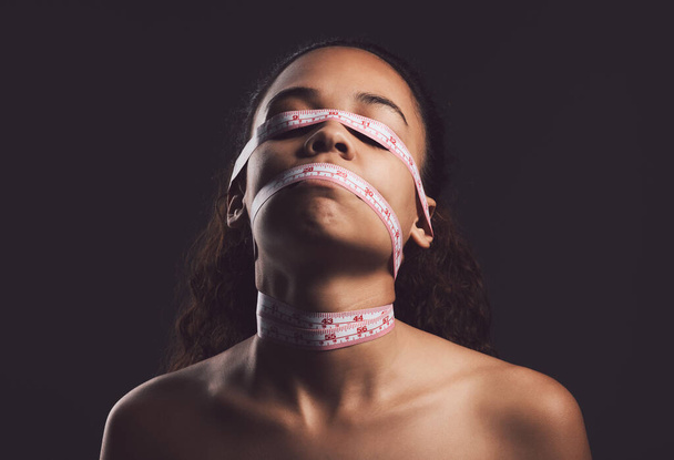 You should love yourself. A young woman wrapped in measuring tape against a black background - Photo, Image