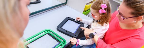 Non-verbal girl living with cerebral palsy, learning to use digital tablet device to communicate. People who have difficulty developing language or using speech use speech-generating devices. - Photo, image