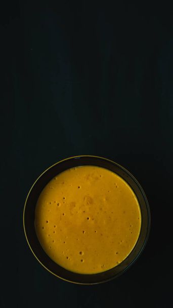 tazón de cerámica amarillo y negro lleno de puré de calabaza sobre un fondo negro. Foodie. retrato imagen - Foto, Imagen