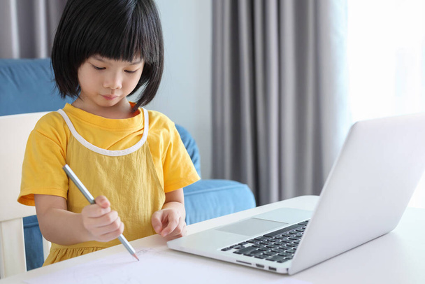 小さなアジアの女子学生は自宅のノートパソコンを使ってオンラインで勉強し - 写真・画像