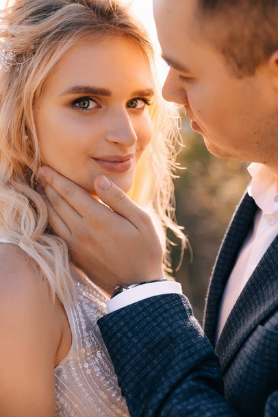 Detailní záběr portrét veselý mladý svatební pár, dívka se dívá do kamery, zatímco ženich se dotýká nevěsty tvář rukou.. - Fotografie, Obrázek