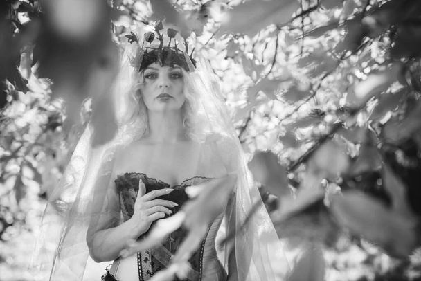 Mariée d'Halloween en corset rose, couronne de fleurs gothiques et voile sur fond nature, tenues pour fête - Photo, image