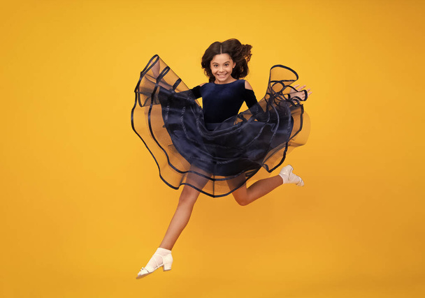 Full length teenager with movement dress. Young teen child with flowing skirt. Teen girl fluttering dress in motion, isolated on yellow. Happy face, positive and smiling emotions of teenager girl - Foto, Bild