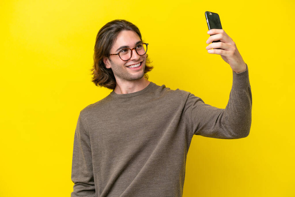 Kavkazský pohledný muž izolované na žlutém pozadí dělat selfie - Fotografie, Obrázek