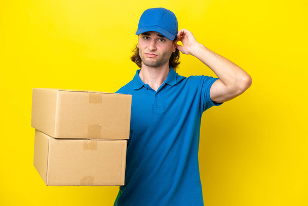 Delivery handsome man isolated on yellow background having doubts - Fotó, kép