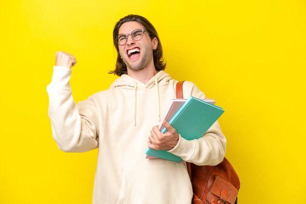 Молодий студент красивий чоловік ізольований на жовтому тлі, святкуючи перемогу
 - Фото, зображення