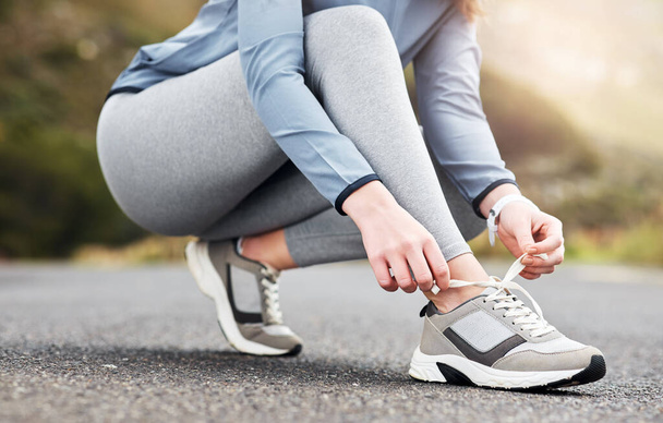 These are so comfortable to run in. a woman tying her shoelaces while out for a run on a road - Fotoğraf, Görsel