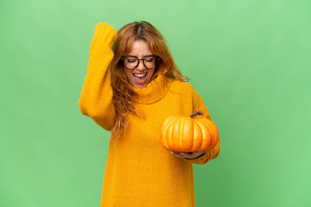 Young caucasian woman holding a pumpkin isolated on green screen chroma key background celebrating a victory - Photo, Image