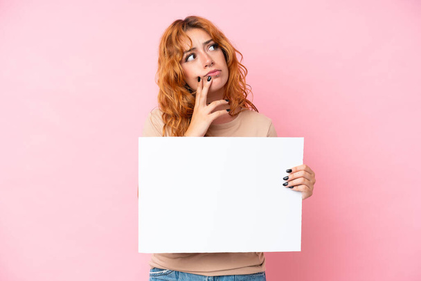 Young caucasian woman isolated on pink background holding an empty placard and thinking - Foto, afbeelding