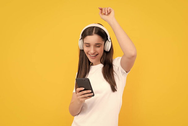 mujer feliz escuchar música en auriculares con teléfono inteligente sobre fondo amarillo, música. - Foto, Imagen