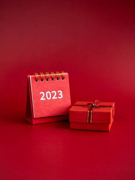 Hyvää uutta vuotta 2023 pystysuora taustoja. 2023 numerot vuosi pieni punainen kirjoituspöytä kalenteri kansi ja pieni lahja laatikko eristetty punaisella taustalla, pystysuora tyyli, minimalistinen. - Valokuva, kuva